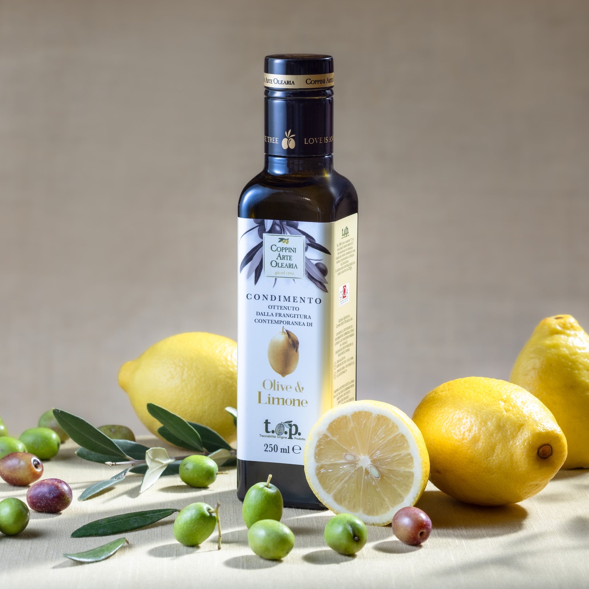 bottiglia di olio al limone Coppini Arte Olearia in mezzo a olive e limoni freschi